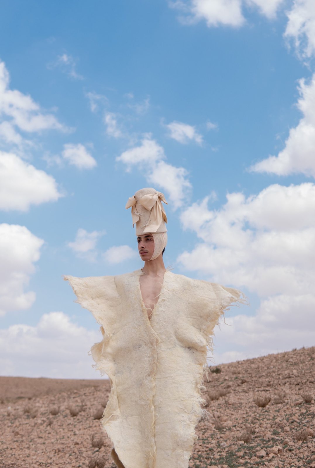 A single figure in a raw fleece cape in the desert.