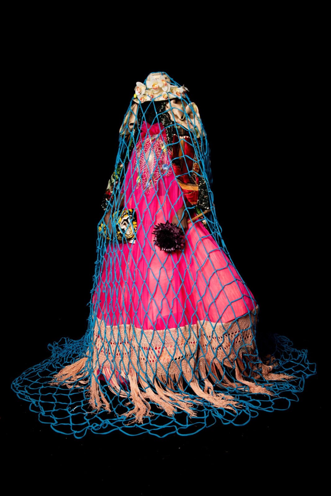 A hot-pink gown veiled under a turquoise net and orchids, on black.