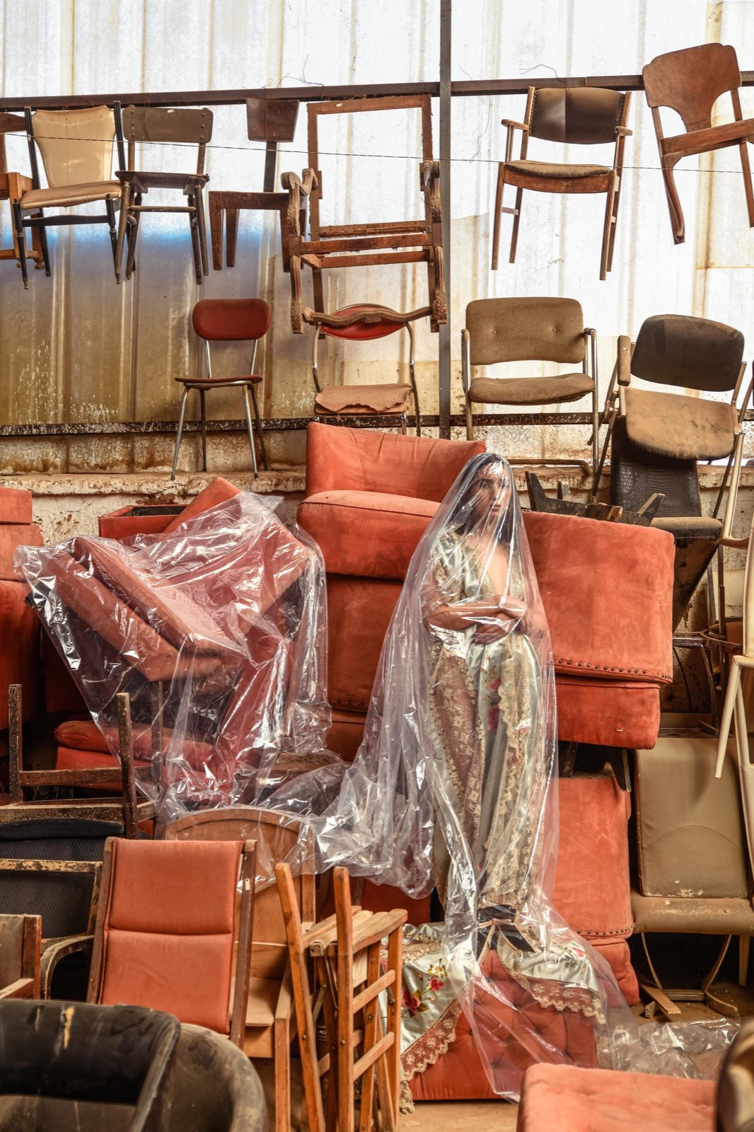 A veiled Maison ARTC figure among a warehouse of stacked terracotta velvet chairs, Marrakech.