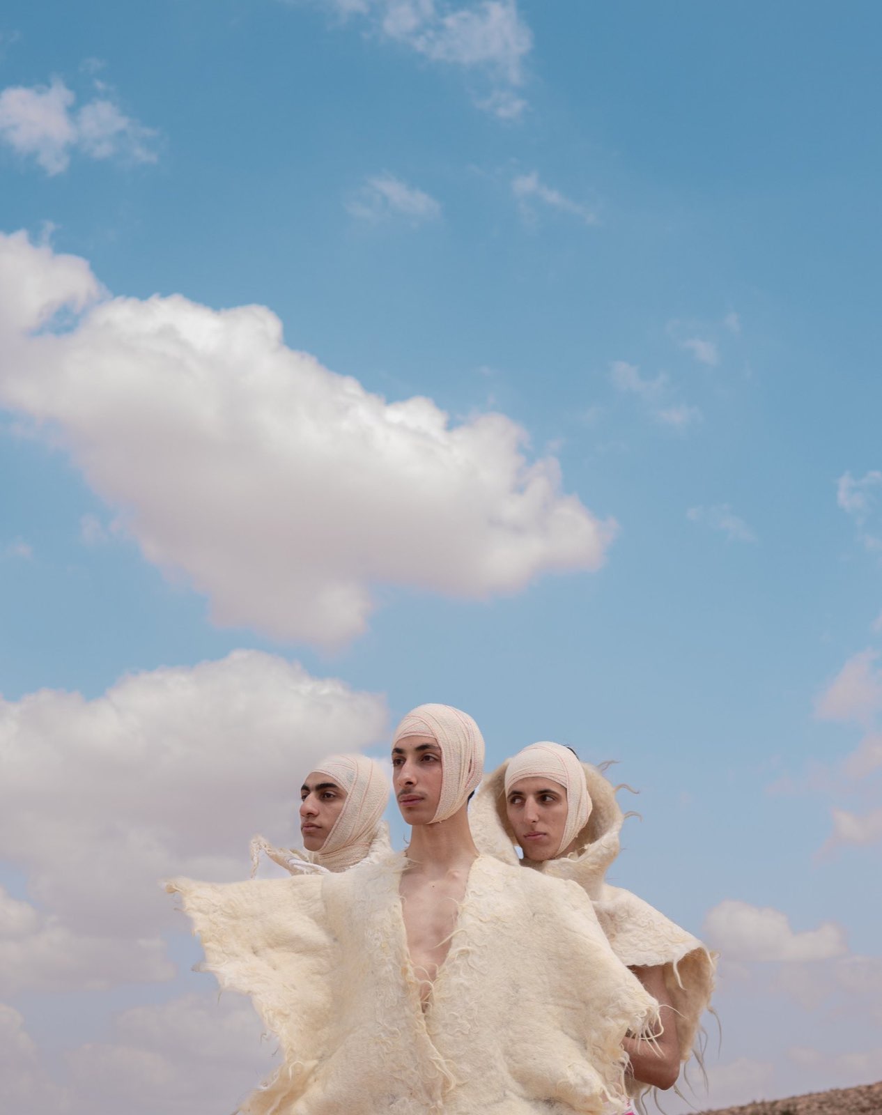 Three men in bandaged hoods and raw fleece against the sky.
